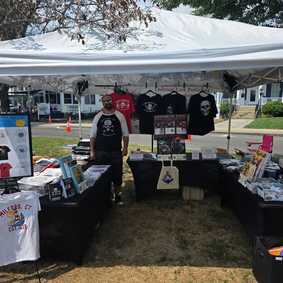Outdoor tent booth with shirts and prints, Dan standing behind the table