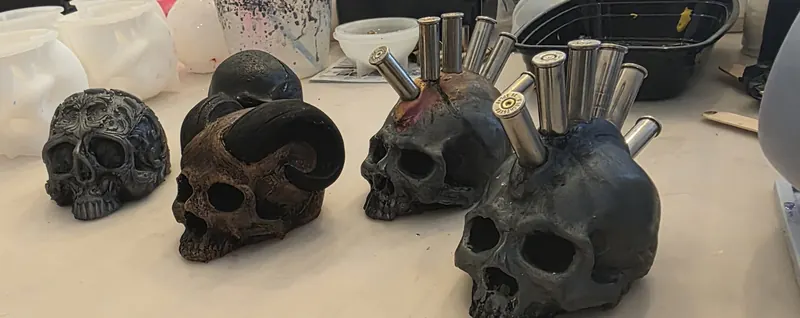 Four black cast resin skulls, two holding paintbrushes and pens