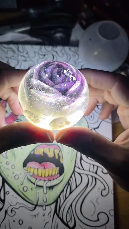 Resin sphere with a violet rose inside, glowing between two hands